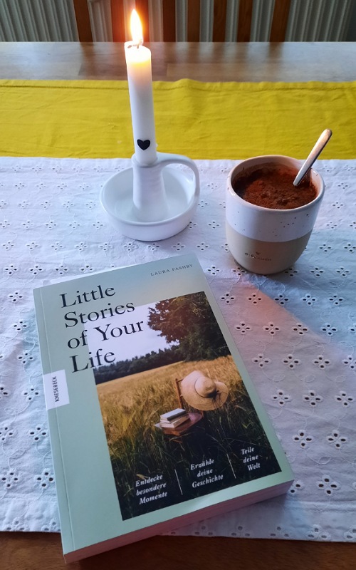 Kerze, Kakao und Buch auf einem Tisch